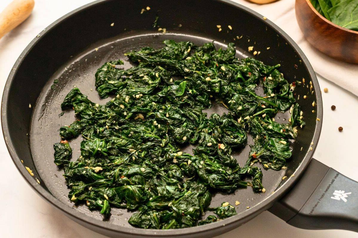 Sautierter Spinat mit Knoblauch und Zitrone in der Pfanne nach dem Welken.