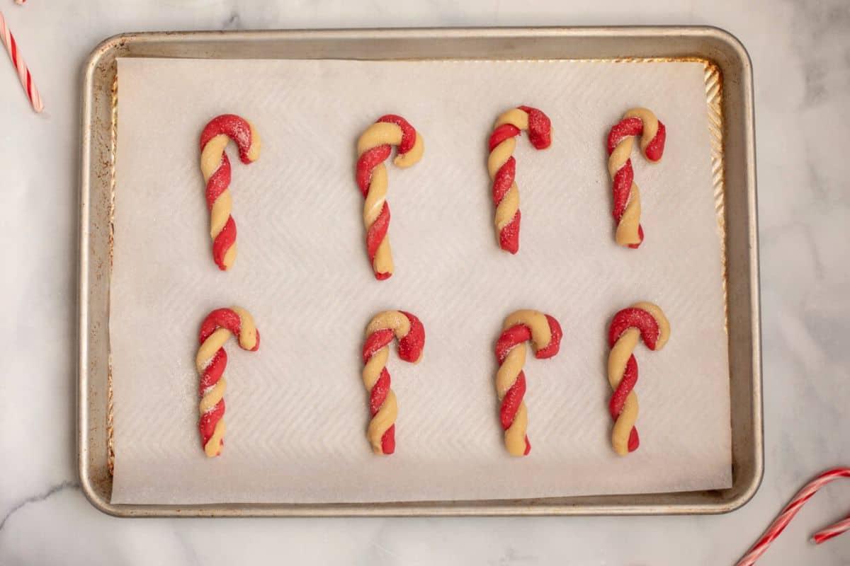 Geformte Zuckerstangen-Plätzchen auf dem Backblech, bestreut mit Glitzerzucker.