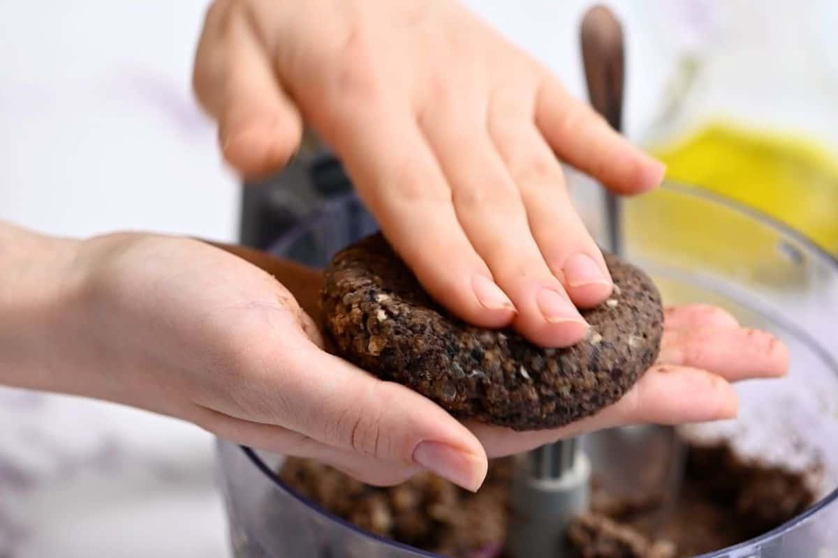 Hände formen schwarzen Bohnenburger zu einem Burger-Patty.