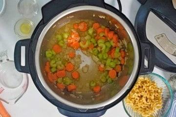 Der Innentopf des Instant Pots nach dem Ablöschen mit Weißwein, mit angebratenen Karotten, Zwiebeln, Sellerie und Knoblauch. Zutaten für die Puten-Nudelsuppe sind im Hintergrund.