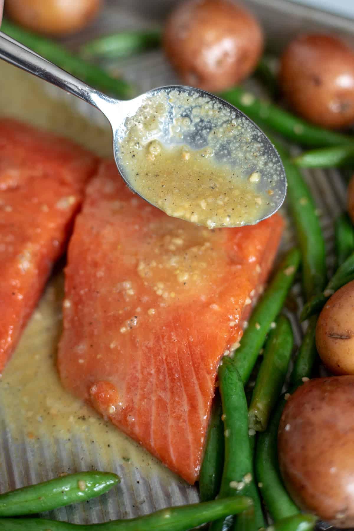Löffel gießt Glasur über Lachsfilet auf dem Backblech.