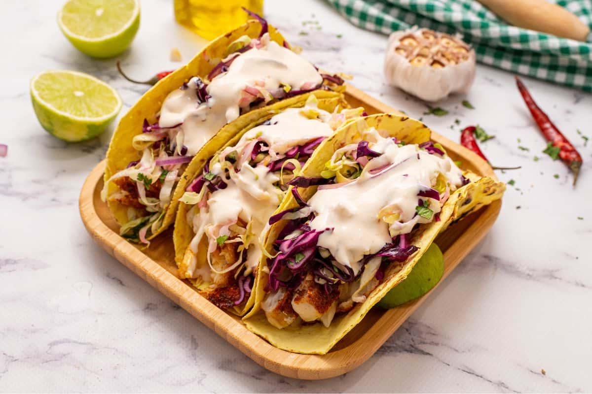 3 Fisch Tacos serviert mit Krautsalat und Soße auf Maistortillas.