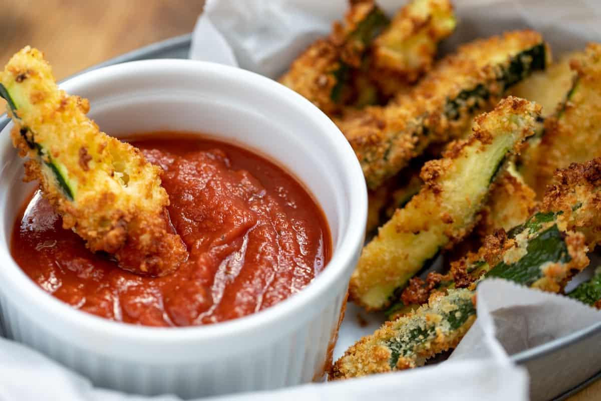 Parmesan Zucchini Pommes in einem Korb, eine davon in Marinara-Sauce getaucht.