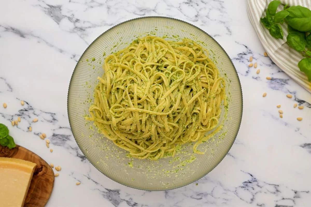 Gekochte Linguine Nudeln mit hausgemachtem Basilikumpesto in einer Schüssel vermengt. Das Pesto umhüllt die Nudeln perfekt.