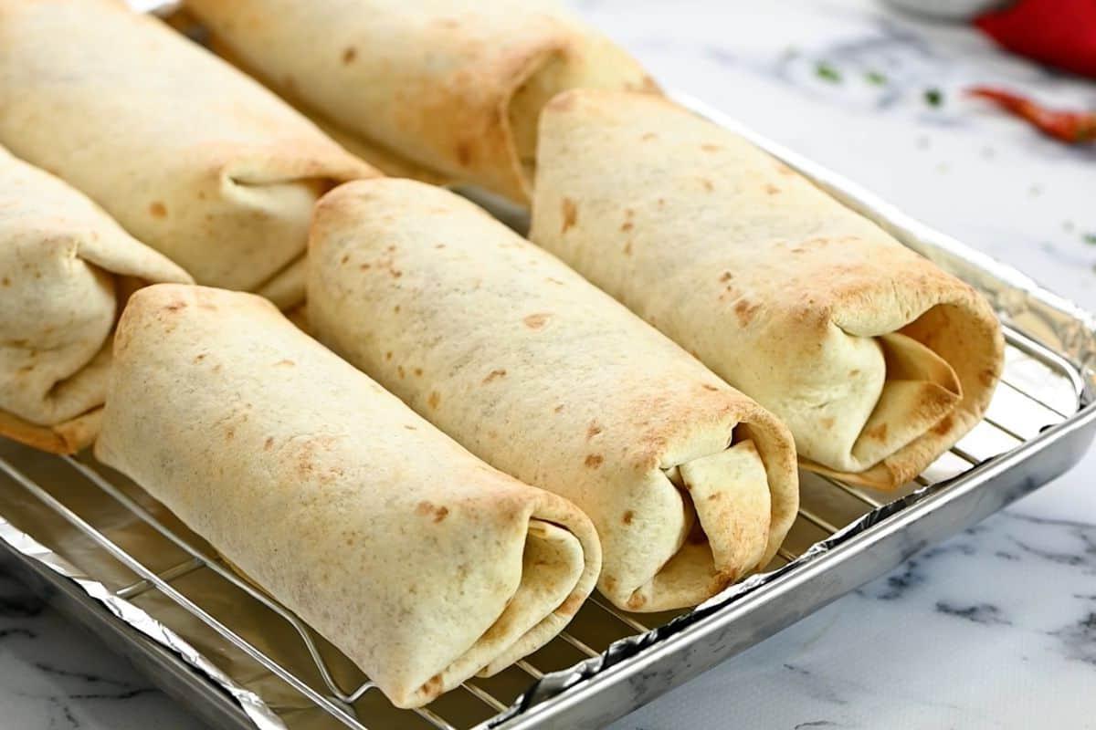 Gebackene Bohnenmus-Burritos auf einem Gitterrost über einem Backblech.