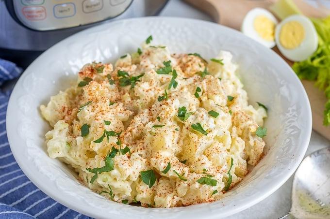 Weiße Schüssel gefüllt mit Instant Pot Kartoffelsalat, hartgekochten Eiern und Sellerie im Hintergrund.