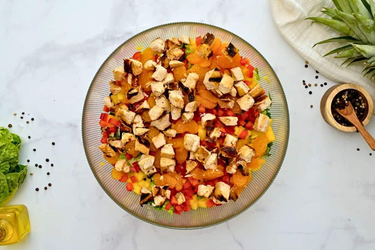 Angemachter Salat mit Orangen-Dressing, Ananas, roter Paprika, Mango und Hähnchen in einer Salatschüssel geschichtet.