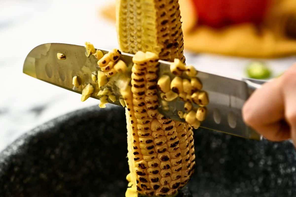 Messer schneidet Mais vom Kolben in eine Gugelhupfform.