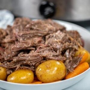 Nahaufnahme des Schmorbratens aus dem Slow Cooker auf einer weißen Platte mit Kartoffeln und Karotten.