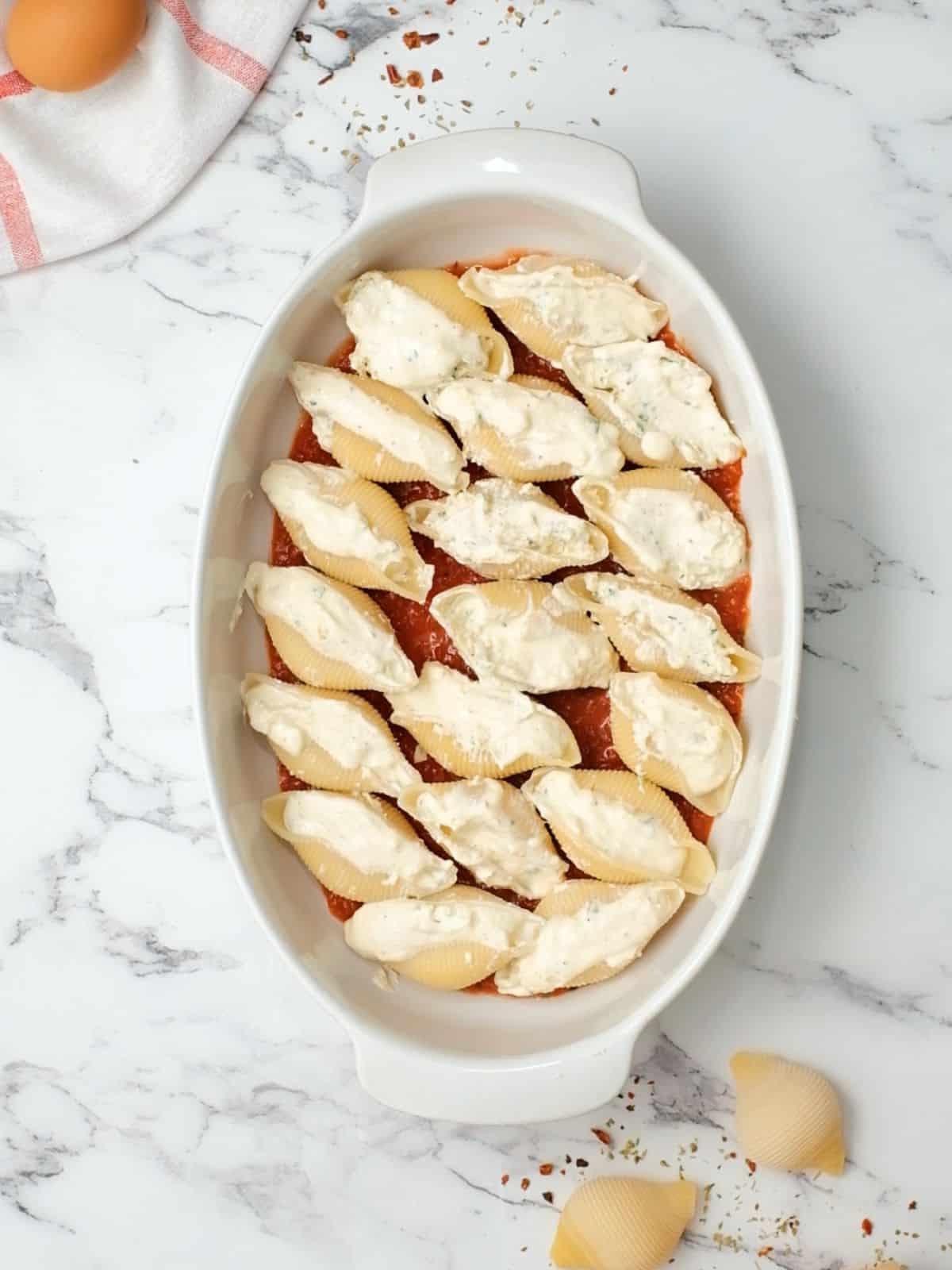 Die besten italienischen gefüllten Nudelschalen 3 Gefüllte gekochte Riesen-Nudelschalen in einer Auflaufform, ausgelegt mit Spaghettisauce.