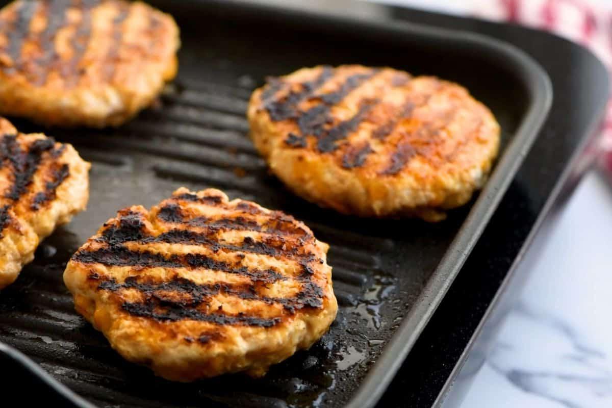 Four chicken burgers on grill plate.