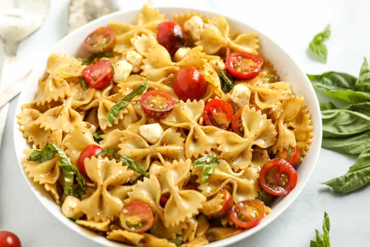 Schüssel Caprese Nudelsalat angerichtet neben frischem Basilikum.