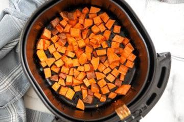 Heißluftfritteusenkorb mit gewürzten Kartoffeln, die auf dem Boden des Behälters ausgebreitet sind.