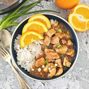 Instant Pot Orangen-Hähnchen serviert mit Reis und frischen Orangen im Hintergrund.