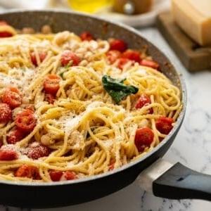 Große Pfanne mit Pasta, weißen Bohnen, Tomaten und Spinat, mit Parmesan bestreut.