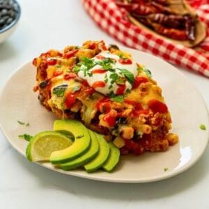 Cowboy Hähnchen 2 Cowboy Hähnchen Auflauf auf weißem Teller serviert, mit Sauerrahm, Koriander, Avocadoscheiben und Limettenspalte.