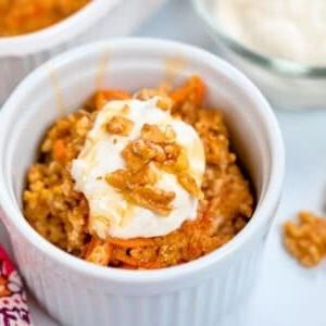 Karottenkuchen-Haferflocken-Auflauf in einer kleinen weißen Schüssel angerichtet, garniert mit griechischem Joghurt, Ahornsirup und gehackten Walnüssen.