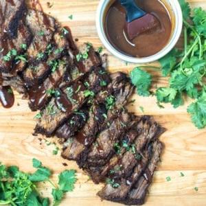 Geschnittenes Instant Pot Brisket auf einem Holzschneidebrett, beträufelt mit BBQ-Sauce und Petersilie an der Seite.