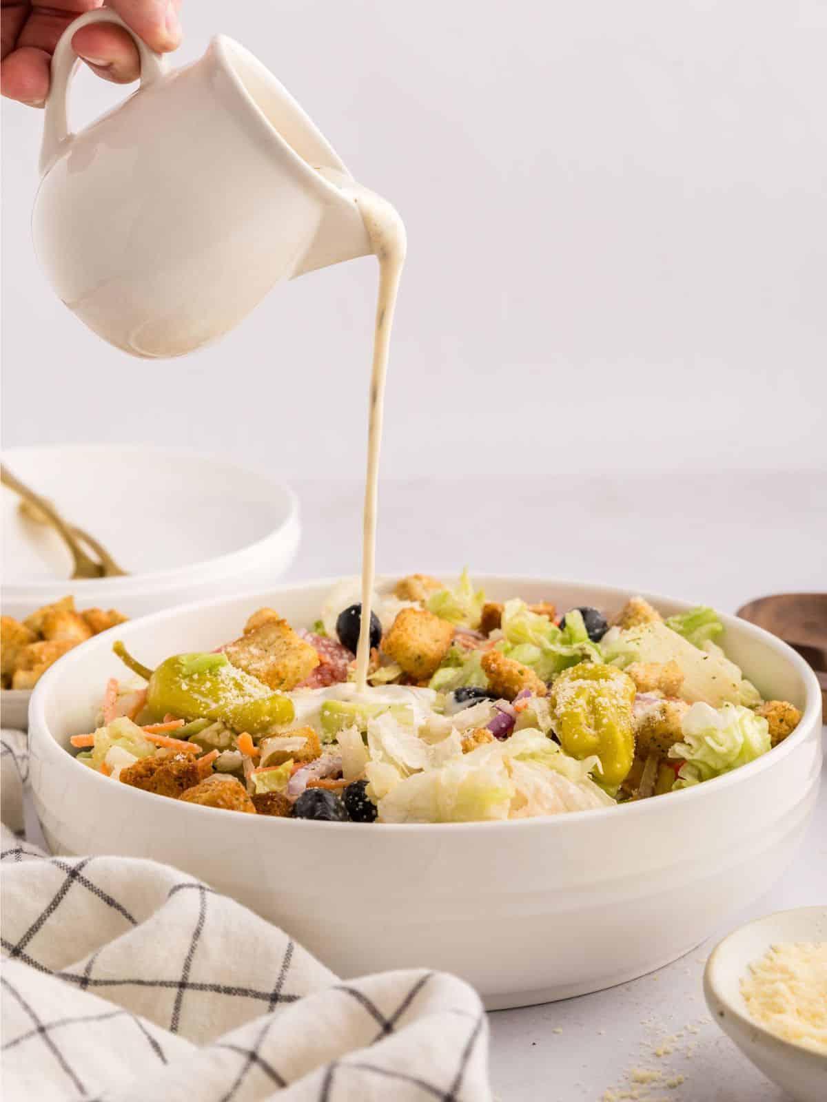 Cremiges italienisches Dressing wird über Eisbergsalat in einer weißen Rührschüssel gegossen.