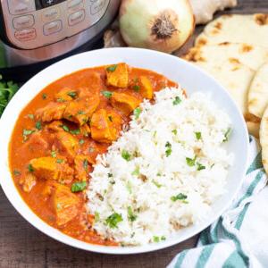 Eine Schüssel Instant Pot Butter Chicken mit Reis neben dem Instant Pot.