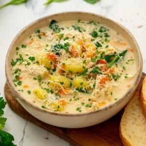 Schüssel mit cremiger Instant Pot Hähnchen-Gnocchi-Suppe neben knusprigem Brot und frischer Petersilie.