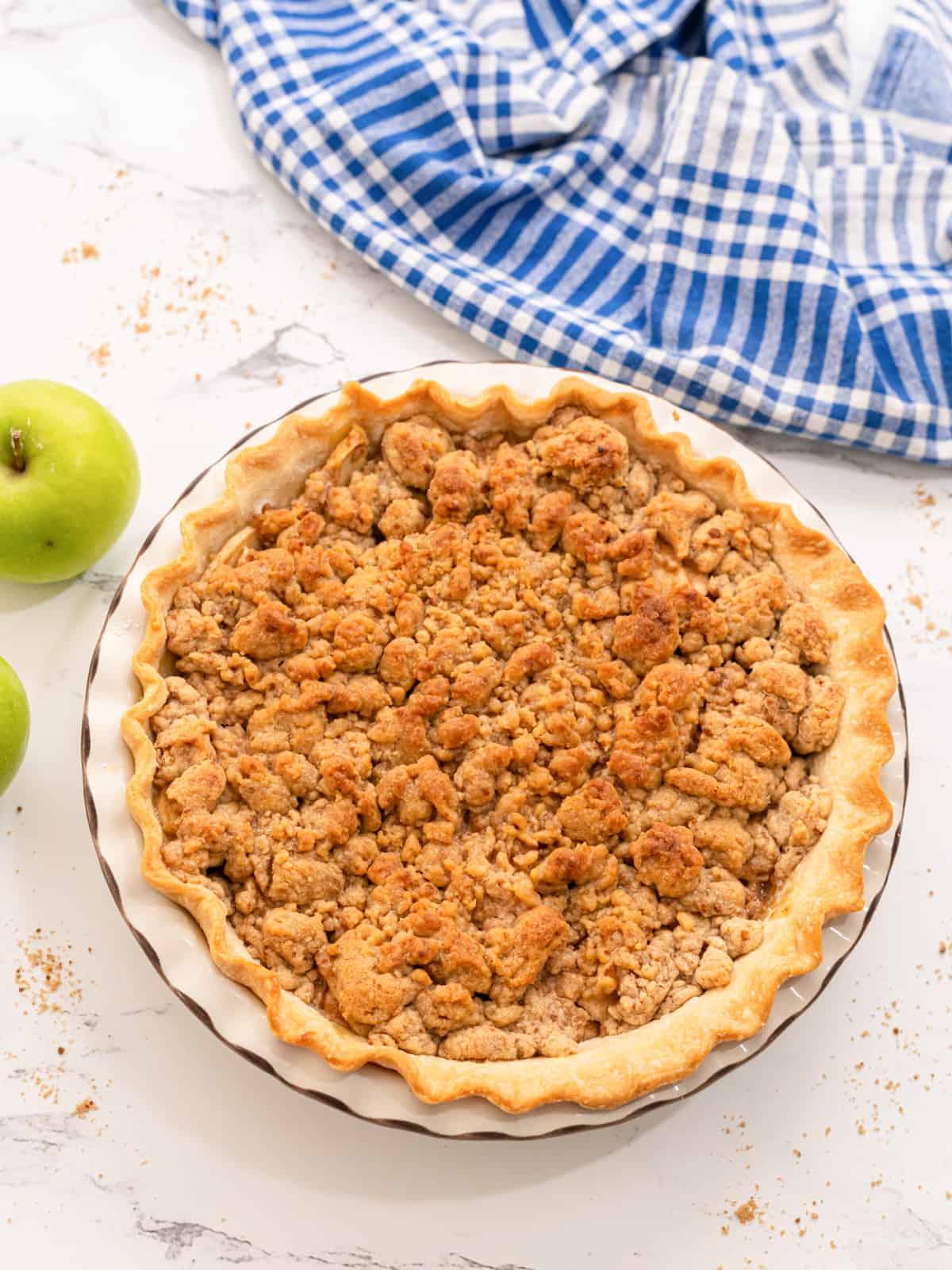Gebackener holländischer Apfelkuchen neben Granny Smith Äpfeln.