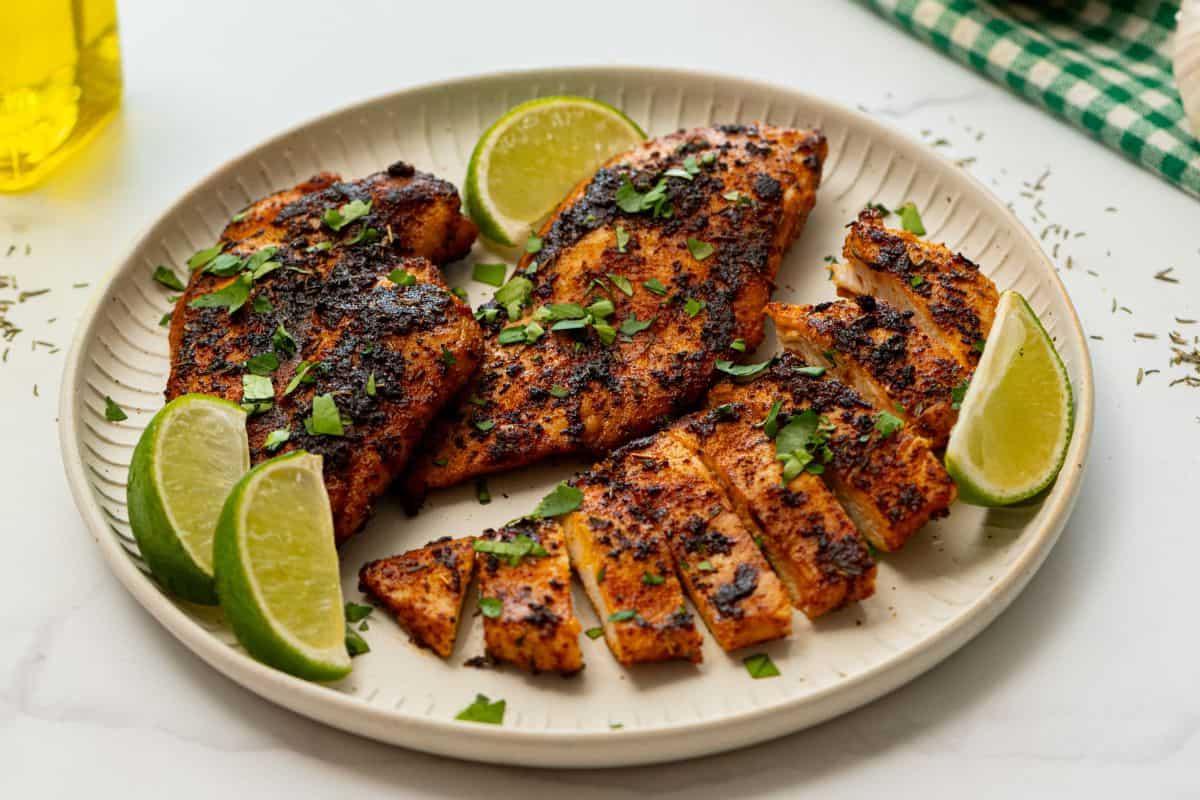 Blackened Chicken Breast on plate with minced cilantro and wedges of limes.