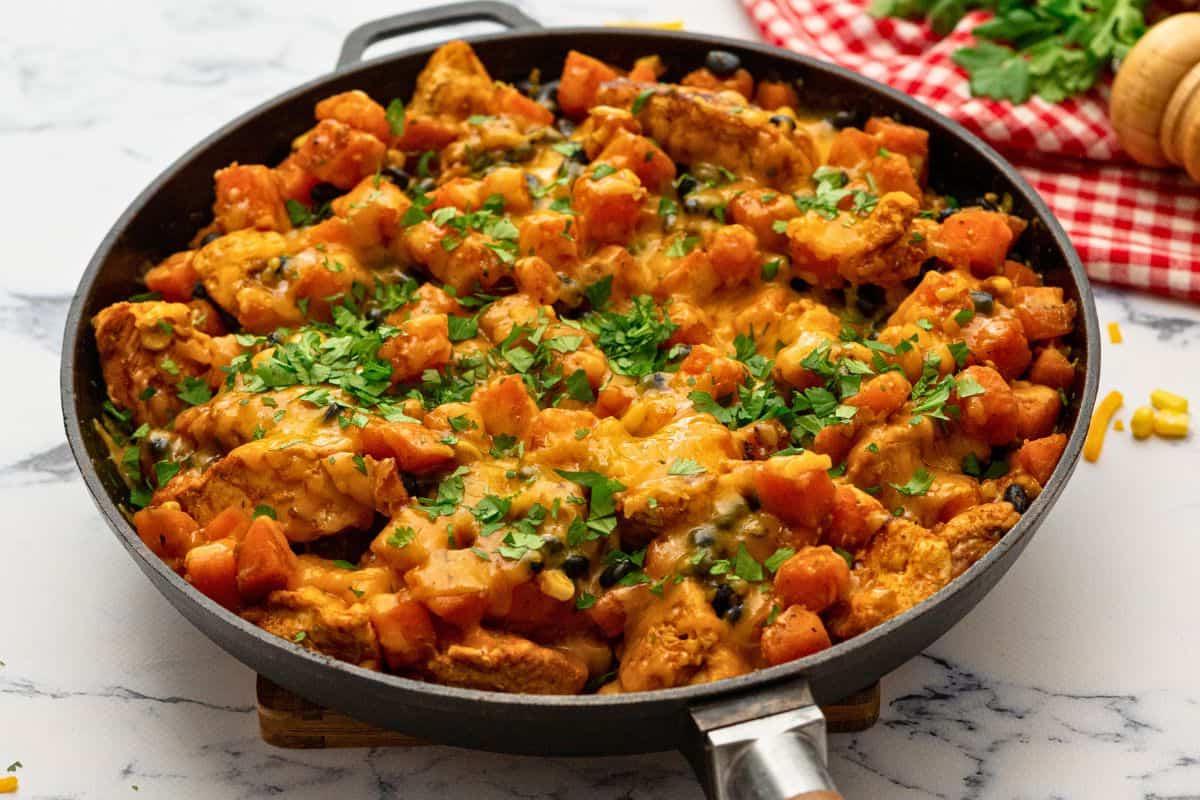 Käsige Hähnchen-Süßkartoffel-Pfanne mit Bohnen und Mais in der Pfanne, mit Koriander belegt.