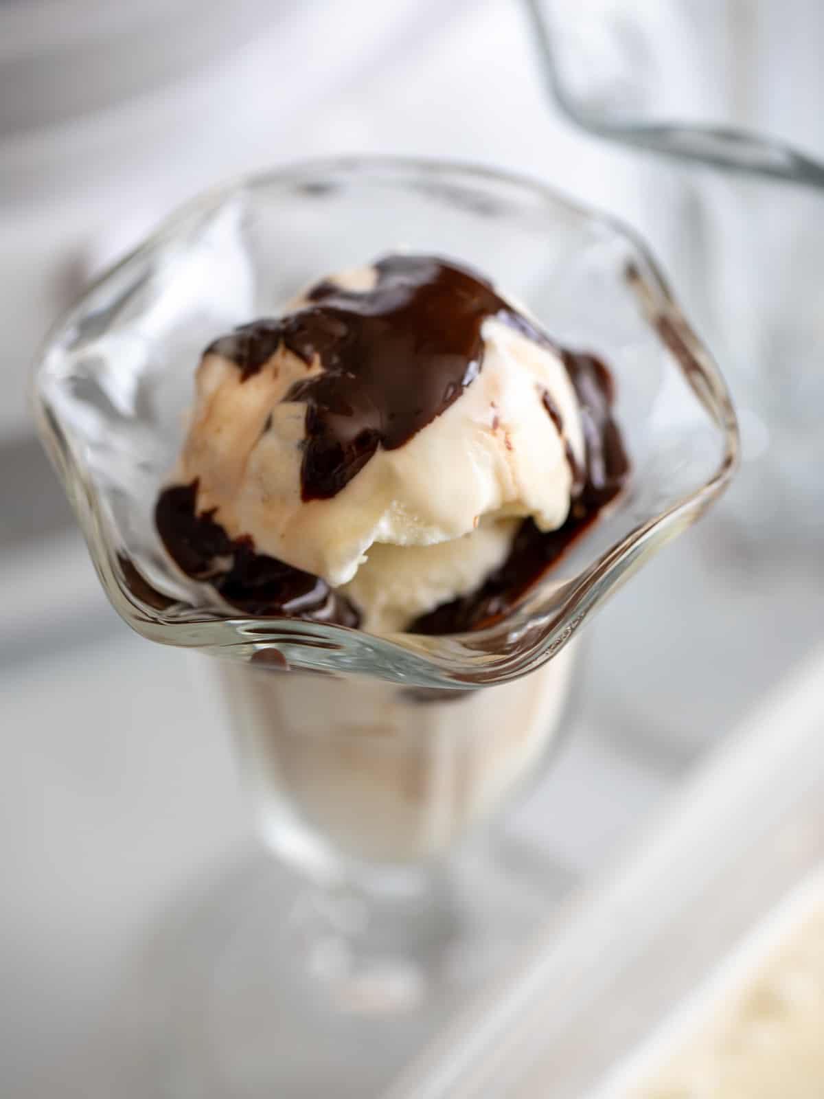 Hausgemachtes Vanilleeis Rezept – Servierfertig Hausgemachtes Vanilleeis in einer ansprechenden Eisbecher-Schale, reichlich mit Hot Fudge garniert – ein wahrer Genuss!