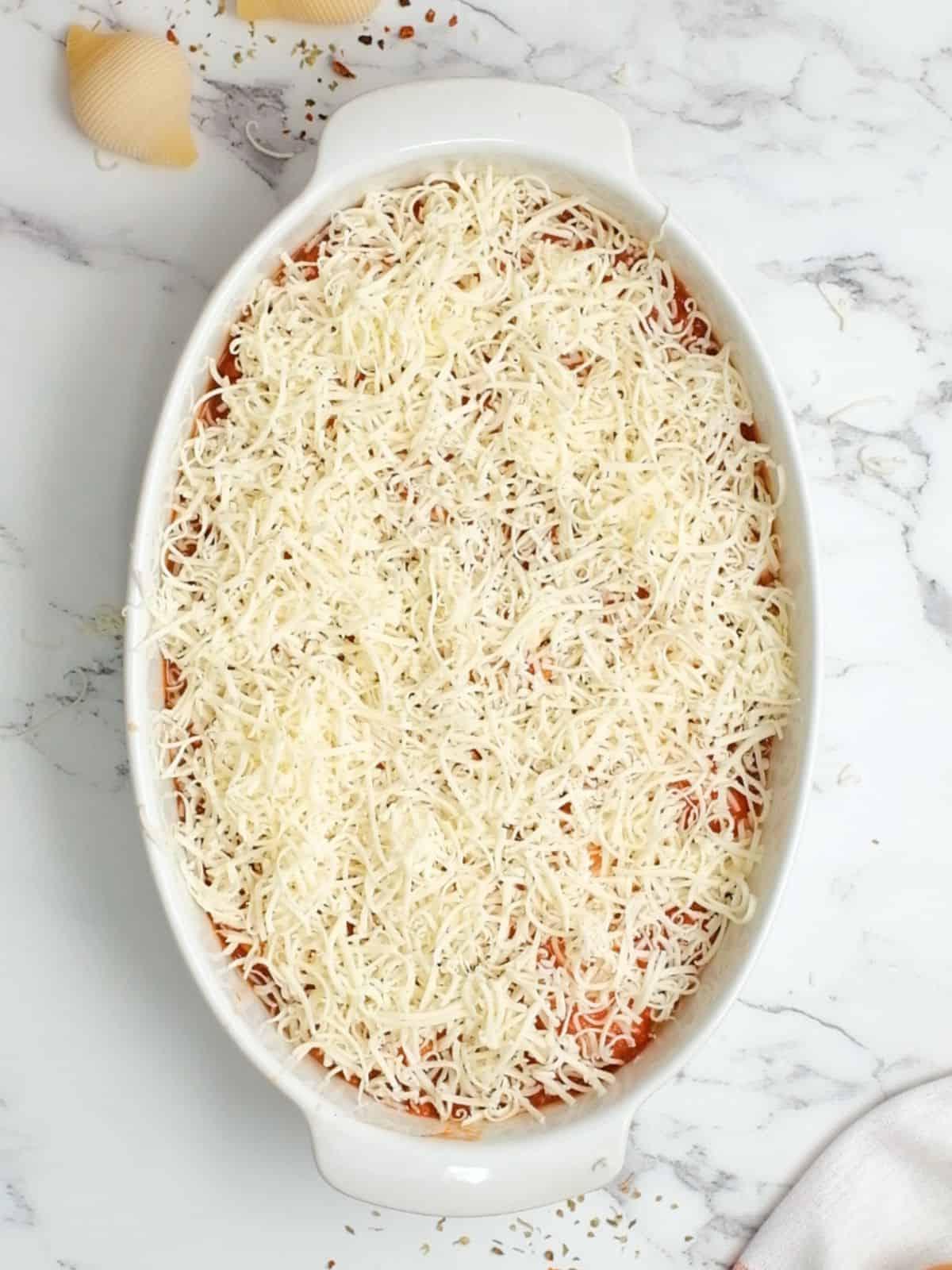 Die besten italienischen gefüllten Nudelschalen 4 Gefüllte Muscheln, belegt mit Marinara-Sauce und geriebenem Mozzarella in einer ovalen Auflaufform.