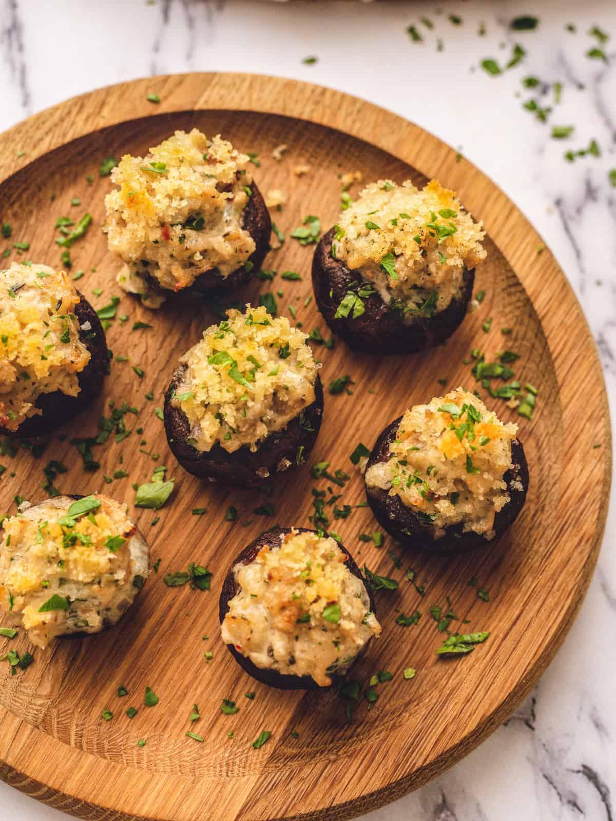 Gefüllte Champignons mit Wurst Gefüllte Champignons mit Wurst- und Paniermehl-Topping auf einer hölzernen Servierplatte.