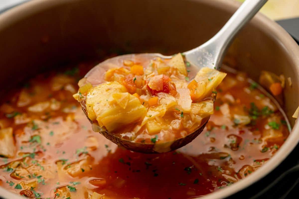 Instant Pot Kohlsuppe servieren Schöpfkelle entnimmt vegetarische Kohlsuppe aus dem Instant Pot.
