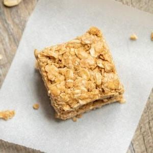 Erdnussbutter-Haferflocken-Riegel auf Backpapier neben einem Blech mit Snackriegeln.
