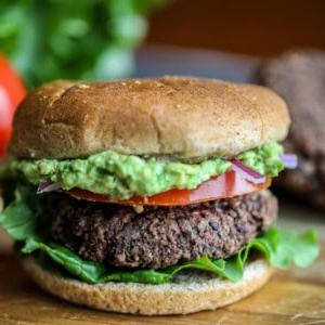 Schwarzer Bohnenburger mit zerdrückter Avocado auf Schneidebrett