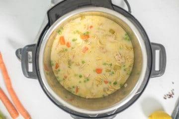Cremige Puten-Nudelsuppe im Innenbehälter des Instant Pots, umgeben von vorbereiteten Karotten- und Selleriestücken.