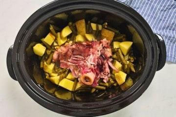 Slow Cooker mit Schinkenknochen, Kartoffeln und grünen Bohnen darin.