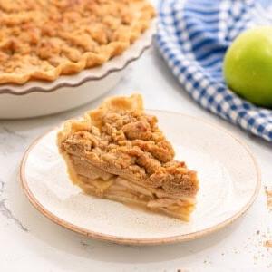 Stück holländischer Apfelkuchen auf weißem Teller neben gebackenem Apfelkuchen.