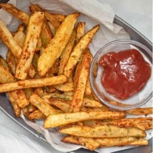 Ein Korb mit hausgemachten Pommes, serviert mit Ketchup, zubereitet in einer Heißluftfritteuse.
