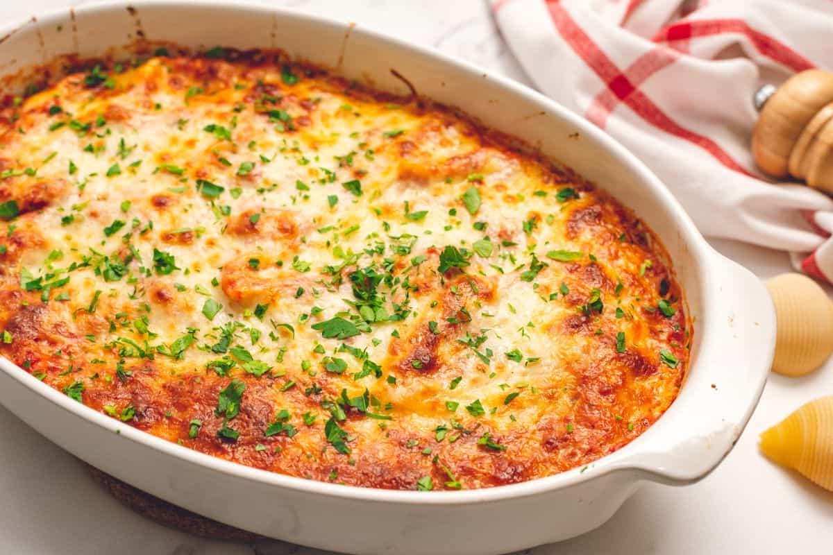 Überbackene mit Ricotta gefüllte Muscheln Überbackene italienische gefüllte Muscheln in einer weißen ovalen Auflaufform, garniert mit frisch gehackter Petersilie.