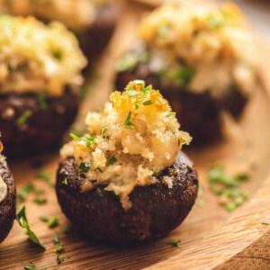 Einfache Wurstgefüllte Champignons 2 Gefüllte Champignons mit Wurst- und Paniermehl-Topping auf einer hölzernen Servierplatte.