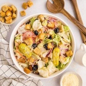 Nachgemachter Olive Garden Salat mit Eisbergsalat-Mischung, Oliven, Tomaten und Croutons in einer großen weißen Servierschüssel neben einer kleinen Schüssel mit Parmesankäse.
