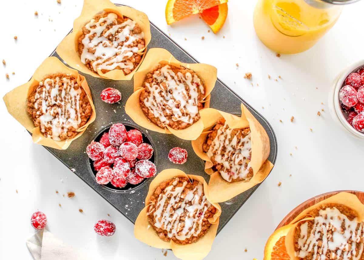 Cranberry-Streusel-Muffins in der Backform neben gezuckerten Cranberries.