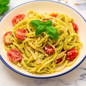 Schüssel Pesto Nudeln mit frischen Tomaten und Basilikum garniert. Perfekt für ein schnelles Abendessen.