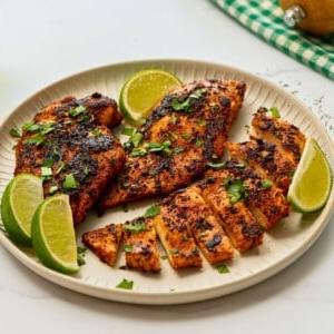 Blackened Chicken Breasts on plate with cilantro and lime wedges.