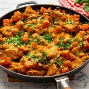 Käsige Hähnchen-Süßkartoffel-Pfanne mit Bohnen und Mais in der Pfanne, mit Koriander belegt.
