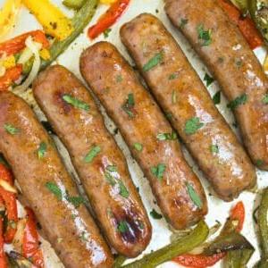 Ofengebackene italienische Würste mit Paprika und Zwiebeln, garniert mit gehackter Petersilie auf einem Backblech.