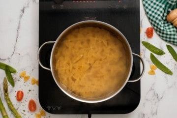 Farfalle Nudeln kochen in einem großen Topf mit kochendem Wasser neben frischem Spargel.