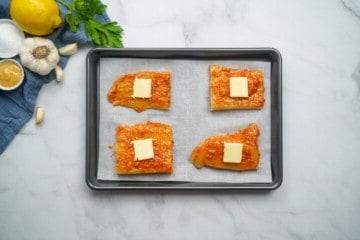 Gewürzter Kabeljau auf einem Backblech mit Butterstücken auf dem Kabeljau.