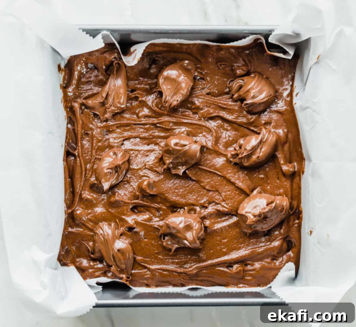 Ζύμη Nutella Brownie σε ταψί 8x8, με κουταλιές Nutella στην κορυφή.