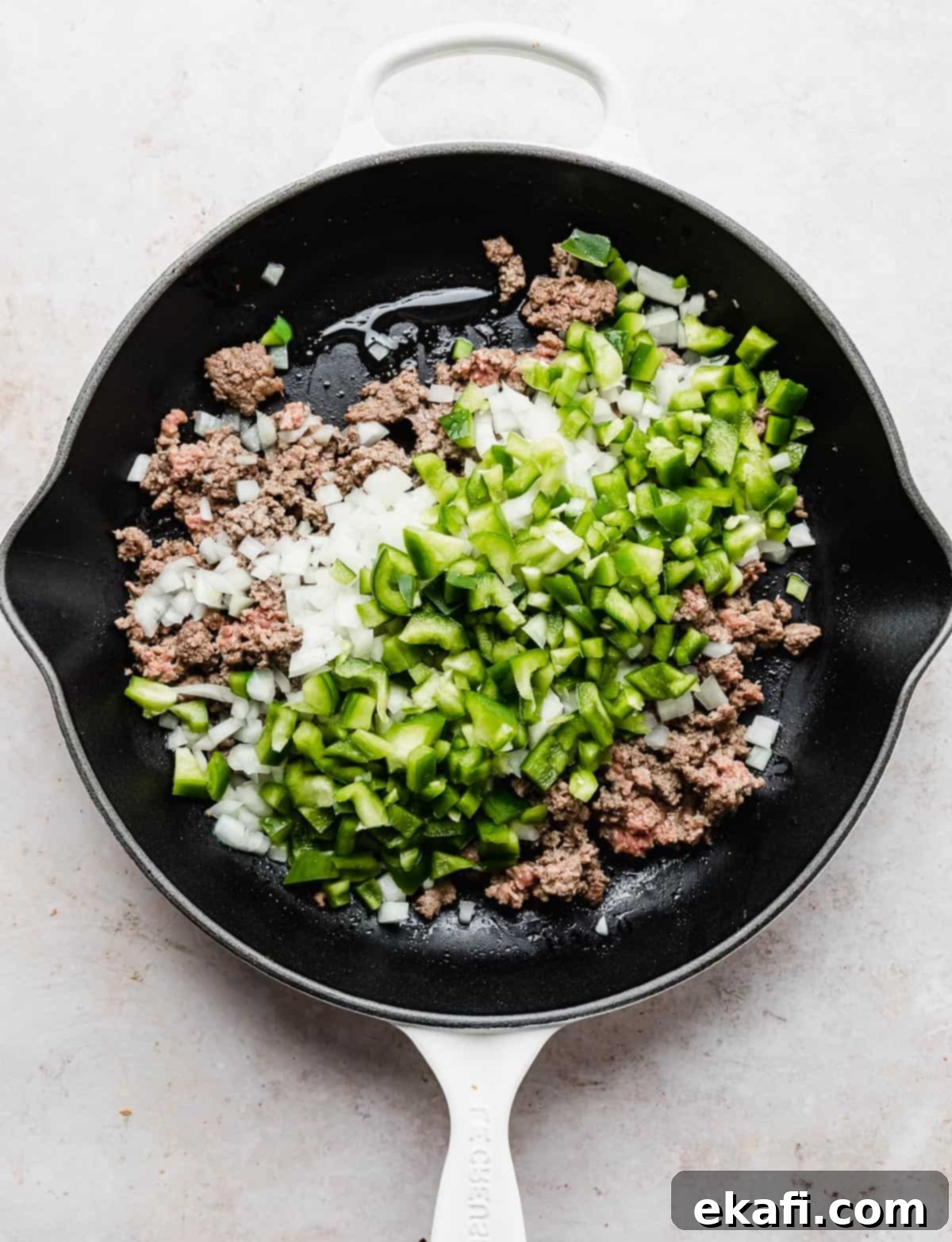 Φιλαδέλφειας Τυρόστεικ Σλόπι Τζο 4 A white skillet with ground beef, chopped onion, and chopped green peppers in it.